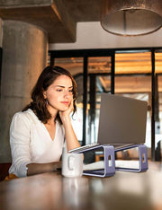 Woman using a laptop on a purple aluminum stand at a cozy desk, showcasing ergonomic design for better posture.